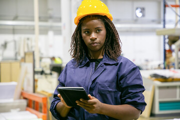 Content female plant worker standing with tablet and looking away. Portrait of pensive African...