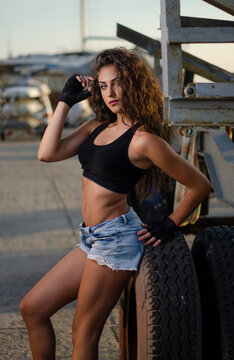 Beautiful athletic woman with curly hair in a black tank top and denim shorts next to a boat