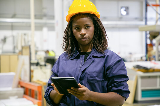 Content Female Plant Worker Standing With Tablet And Looking Away. Portrait Of Pensive African American Woman Doing Her Job, Thinking And Wearing Uniform. Manufacture And Digital Technology Concept