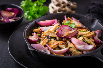Fried mushrooms with onions and herbs on dark background