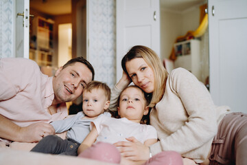 Fototapeta premium Happy family having fun at home. Young blond woman and man hugging their kids lying on the floor in children room. Image with selectie focus and toning