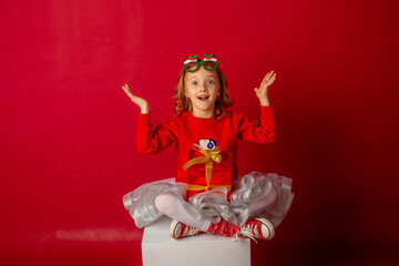 little girl in carnival glasses holds a gift on a red background, christmas