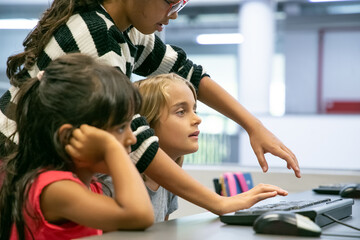 Cropped multiethnic female pupils studying in IT class together. Concentrated lovely children learning in classroom. Hispanic girl typing on keyboard. Informatics and education concept