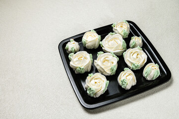 White marshmallows in the shape of a roses laid out in rows on a square black plate. White background.