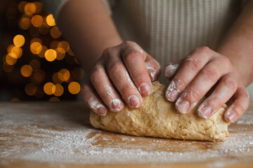 Girl kneading the dough for gingerbread cookies. Christmas tree lights bokeh in background. Female hands preparing dough, baking homemade cookies.