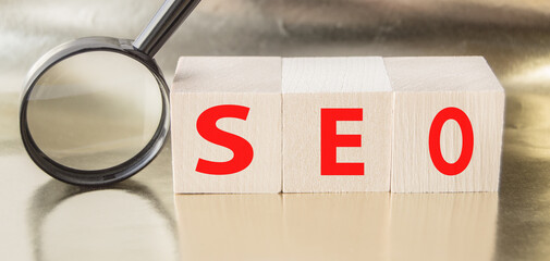 SEO search engine optimization text wooden cubes and magnifying glass on a Golden background. Idea,...