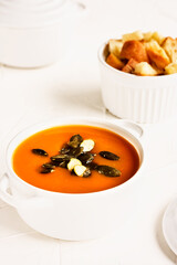 Vegetarian spicy autumn pumpkin cream soup served in white cocotte with croutons and pumpkin seeds on white background.Seasonal autumn vegetarian food