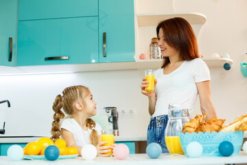 Young beautiful mother and her little daughter playing in the kitchen during breakfast at home.