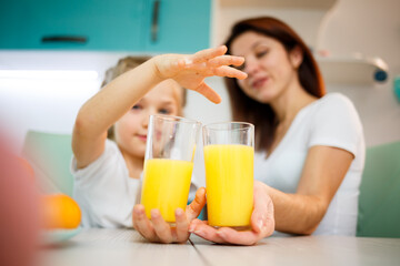 Mother with little girl drinking orange juice while they have breakfast together
