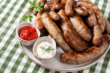 Fried sausages. Bavarian and Nuremberg sausages with spices, sauce, tomatoes and parsley. Delicious meat sausages in a white ceramic plate on a light gray table. German dish
