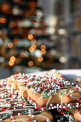 Christmas cookies with red and green in front of a blurred Christmas tree with lights. Vertical image with selective focus and copy space.