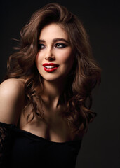 Beautiful bright makeup woman with long brown curly volume brown hair style, red lipstick, and black smokey eyes looking sexy. Closeup