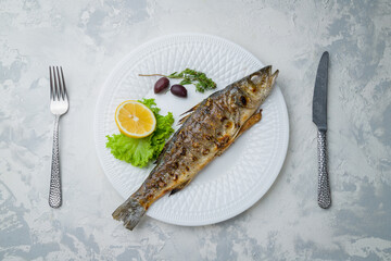 Fried sea bass on the grill, on white plate with lemon