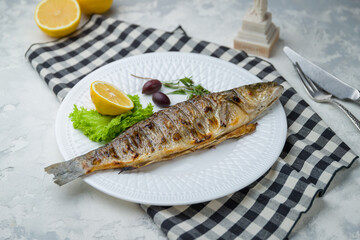 Fried sea bass on the grill, on white plate with lemon