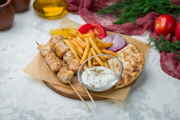 souvlaki with chicken and french fries on board on white concrete table.
