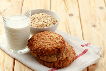 Oat cookies with oat flakes and cup of milk on wooden table