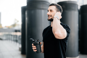 Athletic man pauses training to answer the call. Friendly man talking on the phone with a client while resting after jogging. Morning workout outdoors.