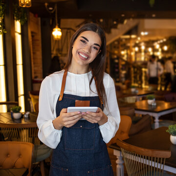 Portrait Of A Beautiful Waitress Working At A Restaurant Using A Tablet Computer And Smiling. Portrait Of A Happy Waitress Working At A Restaurant And Looking At The Camera