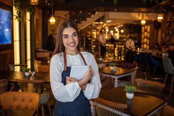 Portrait of a woman working at a restaurant using a tablet computer and looking at the camera smiling - technology concepts.  - Powered by Adobe
