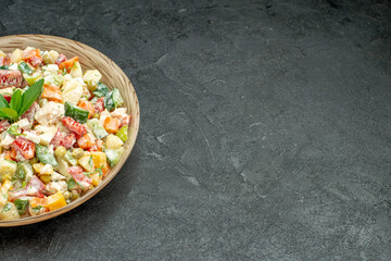 side close view of bowl of vegetable salad on the left side with green on it on dark green background