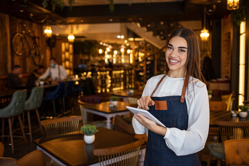 Portrait of a woman working at a restaurant using a tablet computer and looking at the camera smiling - technology concepts. .