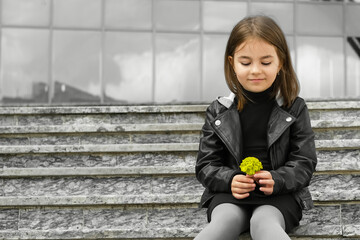 Fototapeta premium Little girl in urban surroundings with yellow flower