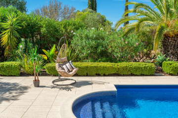 Luxurious pool in the garden of a private villa, hanging chair with pillows for leisure tourists,...