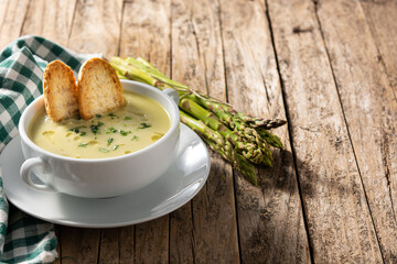 Fresh green asparagus soup in bowl on wooden table. Copy space