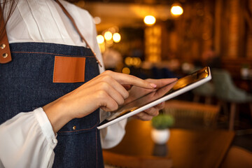 Close-up of female owner standing in her cafe using digital tablet. Female barista standing in coffee shop using digital tablet. Young female owner using digital tablet while standing in cafe