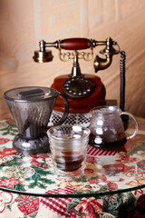 A table in a vintage cafe with a glass of alternatively prepared coffee, coffee gadgets and a vintage telephone