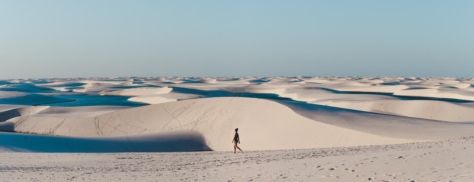 Solo female backpacker walks across the sand dunes of Lencois Maranhenses, miles and miles of sand dunes and lagoons in Maranhao, North-Eastern Brazil