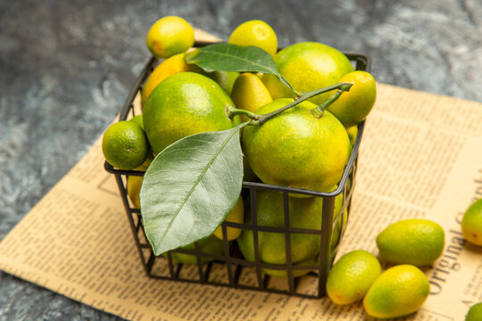 High resolution photo of black basket with fresh green tangerines and kumquats on newspapers on gray background
