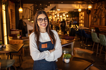 Portrait of a beautiful waitress wearing an apron, smiling at camera. Portrait of positive young woman working professional confectioner in own coffee shop, looking at camera with toothy smile.