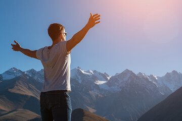 Happy man wearing sunglasses enjoys bright sunshine rays standing against amazing mountain range peaks side view