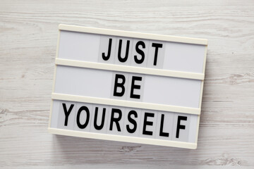 'Just be yourself' on a lightbox on a white wooden background, top view. Flat lay, overhead, from above.