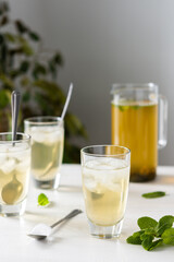 Cold refreshing green tea with ice and mint, tea jug and glasses on white wooden background