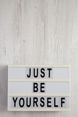 'Just be yourself' on a lightbox on a white wooden surface, top view. Flat lay, overhead, from above. Copy space.
