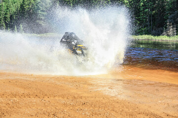 Man driving motocross ATV quad through splashing river lake water with high speed. Foy, Foyross Lake, Sudbury, Canada.