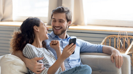 Wide banner panoramic view of overjoyed millennial couple celebrate online win on cellphone...