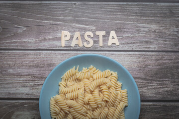 Yummy white fusilli Italian pasta food served on a white plate with pasta wooden letters written