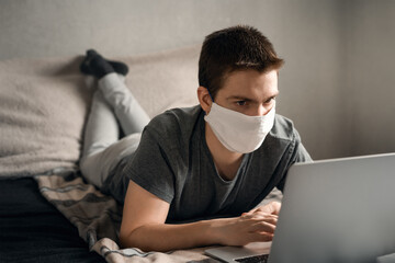 The man in the mask works with the laptop lying on the bed