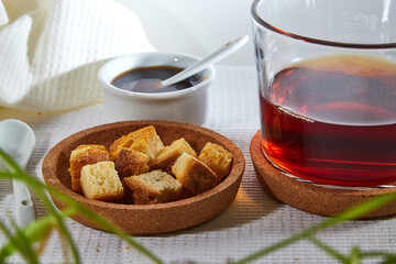 Square toasted pieces of homemade delicious rusk, hardtack, Dryasdust, zwieback, Liquid honey in a saucer and black tee in a cap on a white tablecloth.