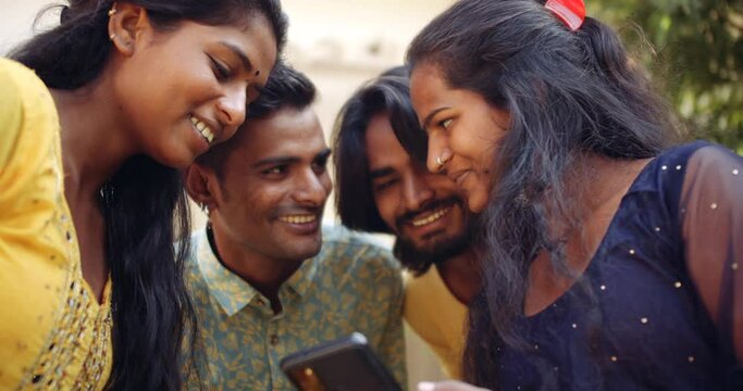 Young Indian adults enjoying themselves as they share a smart phone screen information text message social media profile photo video in slow-motion