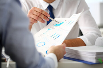 Group of businessmen with financial graph and silver pen in arm solve and discuss problem with...