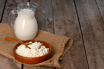 Glass pitcher of milk and bowl of cottage cheese on wooden table