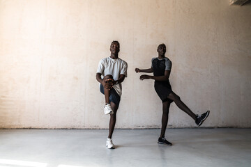 Two young handsome african american men doing workout over wall indoors