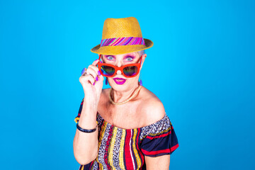 Senior fashionable woman isolated on blue background wearing sunglasses shocked and surprised