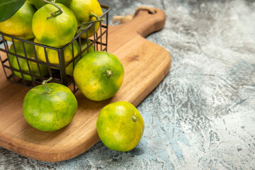 Close up view of green mandarins with leaves inside and outside of a basket on wooden cutting board on gray table