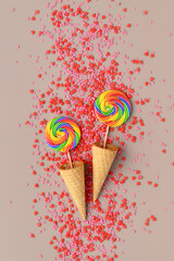 Couple round rainbow lollipops in two waffle cone and pastry topping in heart shape on beige background. Minimal composition, Flat lay, top view, Place for text. Holiday greeting card. LGBT concept