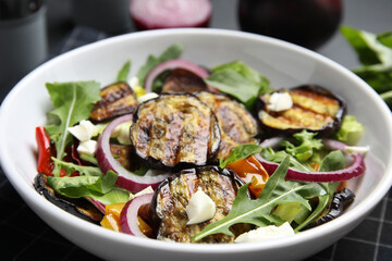 Delicious salad with roasted eggplant, cheese and arugula in bowl, closeup